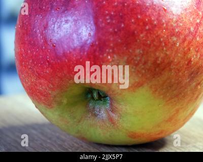 Ein großer roter Apfel auf einer Holzoberfläche, eine Makroaufnahme. Stockfoto