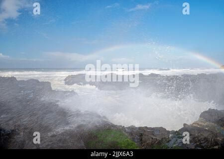 Ozeanspray, das durch Wellen entsteht, die auf Felsen gegen den Himmel krachen Stockfoto