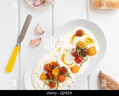 Draufsicht auf Feta Dip mit gerösteten Kirschtomaten auf einem weißen Holztisch Stockfoto