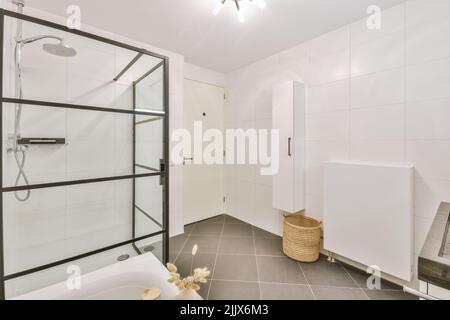 Geflieste Badewanne und transparente Duschkabine befinden sich tagsüber im modernen sonnendurchfluteten Badezimmer zu Hause Stockfoto