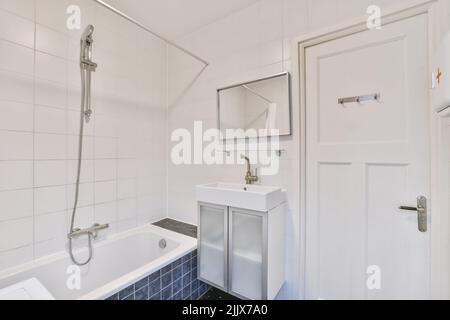 Schrank und Waschbecken mit Spiegel in der Nähe der Keramikbadewanne im modernen Badezimmer mit weißen und blauen Fliesen Stockfoto