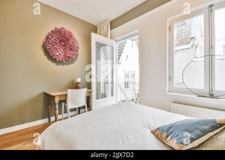 Komfortables Bett mit weichen Kissen und Decke im modernen Schlafzimmer mit Arbeitsbereich Stockfoto