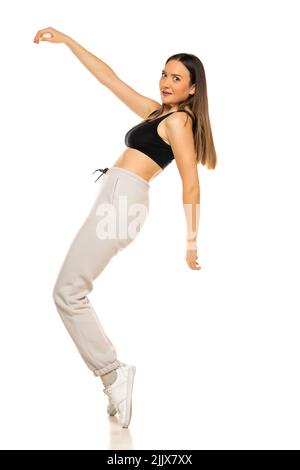 Eine junge Frau in einem grauen Trainingsanzug und schwarzem Oberteil posiert vor weißem Hintergrund im Studio. Stockfoto