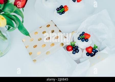 Set aus Pavlova-Baiser-Dessertkuchen mit frischen Erdbeeren und Blaubeeren, dekoriert mit Minze in Geschenkbox verpackt. Süße Präsens Idee. Festliche Foo Stockfoto