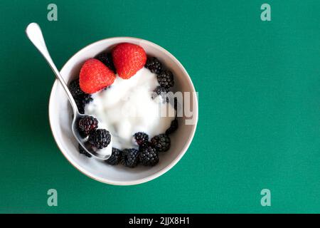Eine kleine Wüstenschüssel voller frisch gepflückter Brombeeren, bedeckt mit fetten griechischen Joghurts und gekleidet mit einer gespaltenen Erdbeere. Eine nahrhafte Mahlzeit Stockfoto