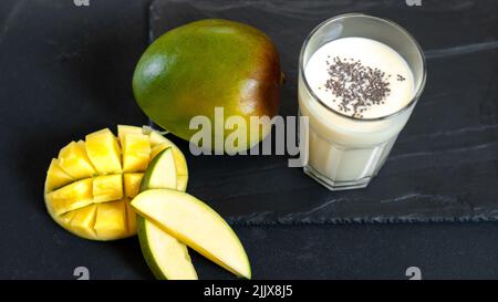 Milchgetränk auf schwarzem Hintergrund mit Mango. Ein klassischer Mango-Milchshake - Lassi. Ein traditionelles Getränk in Indien aus der Hitze. Draufsicht Stockfoto