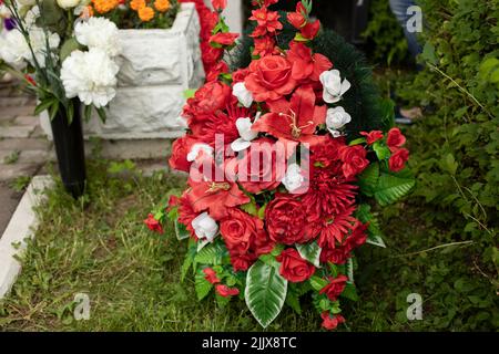 Die Blumen auf dem Grab des Soldaten. Trauerkranz. Rote Kunstblumen. Details der Trauerfeier. Stockfoto