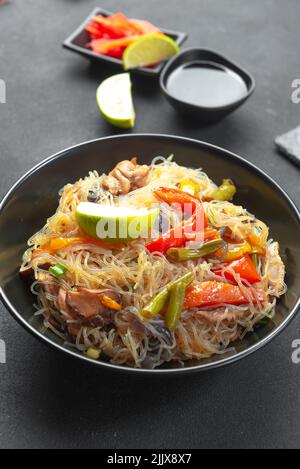 Glasnudel mit Gemüse in einer schwarzen Schüssel auf grauem Hintergrund. Asiatische Küche Asiatische Küche. Asiatische oder Szechuan-Nudeln. Stockfoto