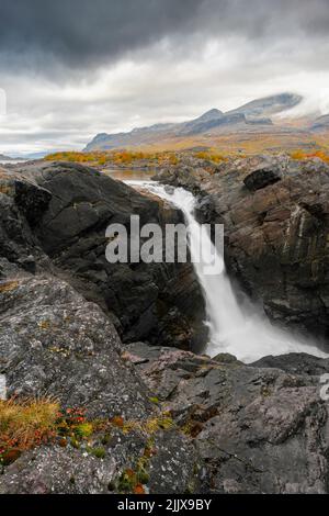 Mächtiger landschaftlicher Wasserfall unter dramatischem Himmel. Stuor Muorkke Wasserfall im Stora Sjofallet Nationalpark, Schweden. Abenteuer in arktischer Wildnis. Herbst Stockfoto