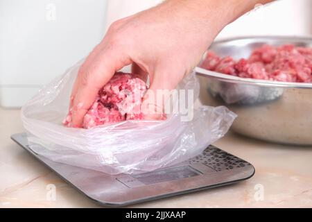 Ein Mann legt portioniertes Schweinefleisch und Rindfleisch in Säcken auf die Waage, um es im Gefrierschrank zu lagern. Stockfoto