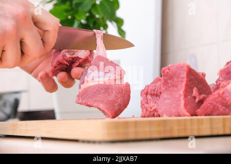 Ein Mann schneidet Fleisch mit einem Messer auf einem Holzbrett. Zubereitung von Hackfleisch und Schweinefleisch für Koteletts, Fleischbällchen, Koteletts. Stockfoto