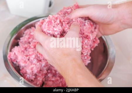 Ein Mann mischt Hackfleisch in einer Schüssel mit seinen Händen. Zubereitung von Hackfleisch und Schweinefleisch für Koteletts, Fleischbällchen, Koteletts. Stockfoto