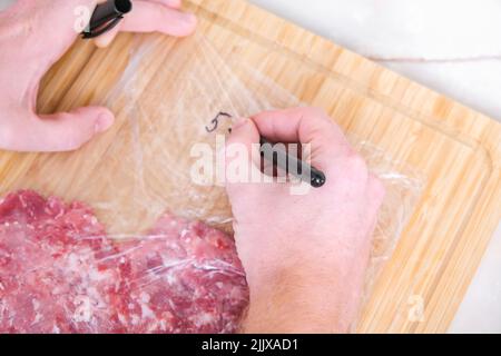 Ein Mann signiert mit einem Marker das Produktionsdatum und ein Gramm gehacktes Schweinefleisch und Rindfleisch, das in Säcken zur Lagerung im Gefrierschrank ausgelegt wird. Produktkennzeichnung. Stockfoto