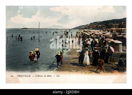 Menschen am Strand des Luxus-Badeortes TROUVILLE, FRANKREICH, um 1904. Vintage-Postkarte gedruckt in Frankreich isoliert auf schwarzem Hintergrund. Stockfoto