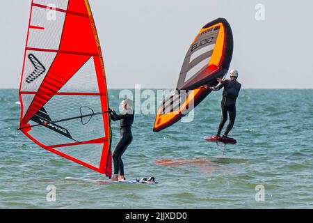 Mädchen / weibliche Freizeit Windsurfer in schwarzem Neoprenanzug üben klassischen Windsurfen und Wingboarder / Wing Boarder Flügel foiling auf See Stockfoto