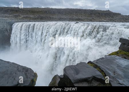 Größter Wasserfall Europas, Dettifoss. Schlammiges Wasser fällt über den Rand. Majestätischer isländischer Wasserfall an einem regnerischen, bewölkten Tag. Stockfoto