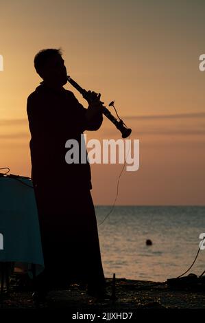 Musiker in Silhouette spielt Instrumente bei Sonnenaufgang am Meer Stockfoto