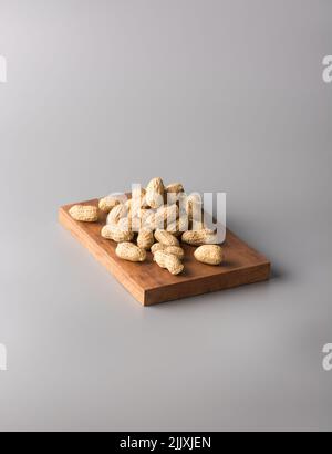 Stapel von ungeschälten Erdnüssen auf einem Holztablett, auch als Erdnuss, Gänseleber, pindar oder Affenmutter bekannt, isoliert auf grauem Hintergrund Stockfoto