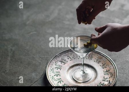 Zwei Hände, die Oliven auf einem silbergrauen Tablett in Martini legen Stockfoto