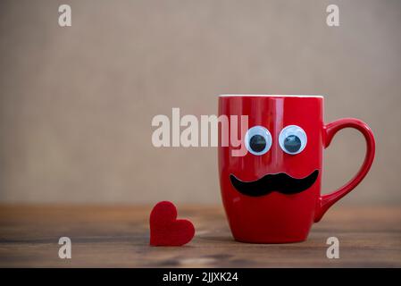 Roter Becher mit Schnurrbart und lustigen Augen, die mit einem roten Herzen aufschauen Stockfoto