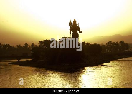 Lord Shiva Statue mit Blick auf Haridwar heilige Stadt in Indien bei goldenem Sonnenaufgang. Gelegen in Ausläufern der Himalaya Berge am Ufer des Heiligen Ganges Fluss. Stockfoto
