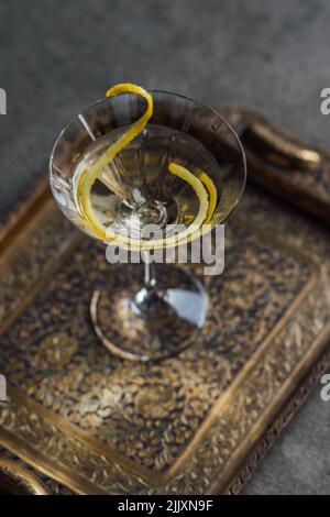 Martini mit einer langen Zitronenverdrehung auf Messingtablett auf Betonboden Stockfoto