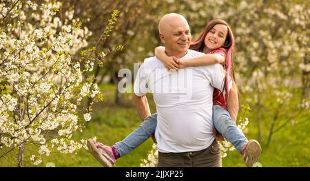 Glückliche Enkelin umarmt ihren lächelnden Großvater auf grünem Rasen Stockfoto