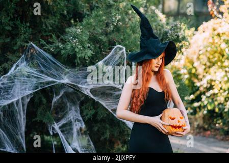 Halloween Hexe Rotschopf Frau macht Hexerei mit magischen Buch der Zaubersprüche, Magie in ihren Händen. Schöne junge Frau in Hexenhut beschwörend. Gruselig Stockfoto