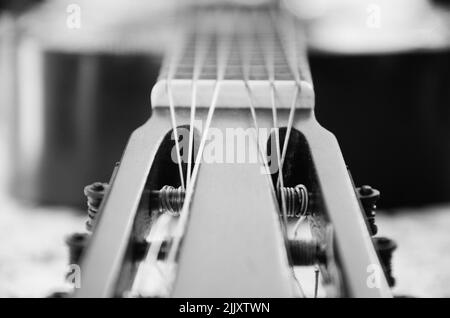 Eine alte spanische Gitarre in schwarz und weiß. Die Saiten sind im Vordergrund zu sehen und der Rest der Gitarre ist aus dem Fokus. Stockfoto