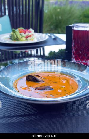 Köstliche Meeresfrüchte Tomatensoße mit Bouillabaisse Fischsuppe mit Garnelen, Muscheln und Fisch auf einem blauen Teller auf dem Tisch. Köstliches romantisches Abendessen in einer Fischruhe Stockfoto