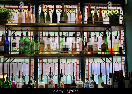 Hinterleuchtete Flaschen auf Regalen in einer Bar mit Buntglasfenster, Großbritannien Stockfoto