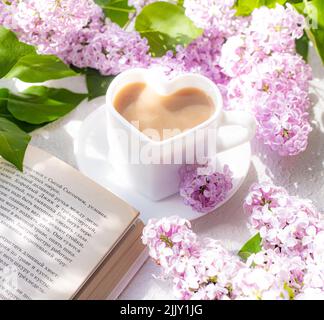 Cappuccino-Kaffee in einer Tasse und einem Zweig von Flieder auf einem weißen Hintergrund mit Schatten . Ein heißes Getränk. Entspannen Sie sich. Das Konzept der Cafeteria-Werbung. Artikel Stockfoto