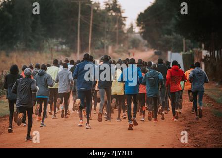 Gruppenausbildung in Kenia. Eine große Gruppe kenianischer Läufer bereitet sich auf das Rennen vor. Ausdauerläufer und Marathonprofis laufen auf dem roten Boden o Stockfoto