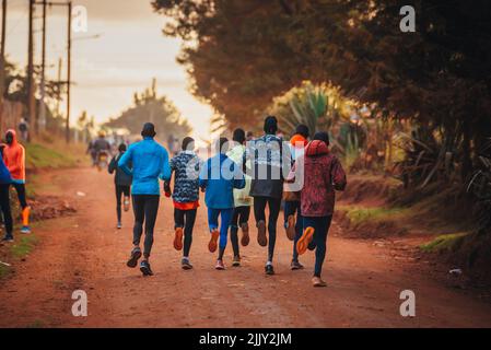Gruppenausbildung in Kenia. Eine große Gruppe kenianischer Läufer bereitet sich auf das Rennen vor. Ausdauerläufer und Marathonprofis laufen auf dem roten Boden o Stockfoto