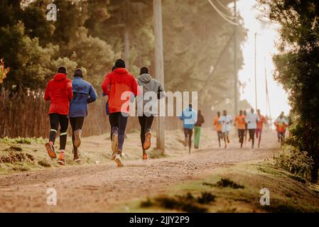 Gruppenausbildung in Kenia. Eine große Gruppe kenianischer Läufer bereitet sich auf das Rennen vor. Ausdauerläufer und Marathonprofis laufen auf dem roten Boden o Stockfoto