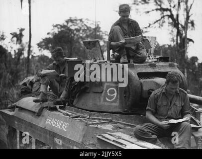Mitglieder einer australischen Panzerbesatzung lasen Post, während sie auf Befehle warteten, sich zur Unterstützung von 3. zu bewegen. Division-Infanterie. Auf Bougainville. 5. Juni 1945. (Foto von Australian Official Photo). Stockfoto
