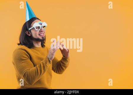 Glücklicher bärtiger Mann mit einer Papierkappe in seinem 30s Geburtstag feiert. Hochwertige Fotos Stockfoto