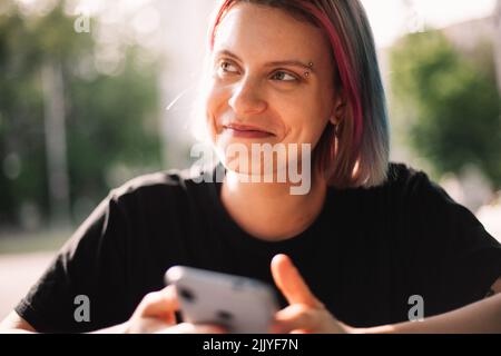 Glückliche junge Frau lächelt und schaut weg und hält Smartphone im Freien Stockfoto