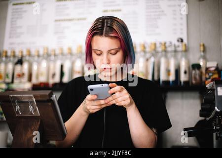 Die Barista benutzt ein Smartphone an der Kasse im Café Stockfoto