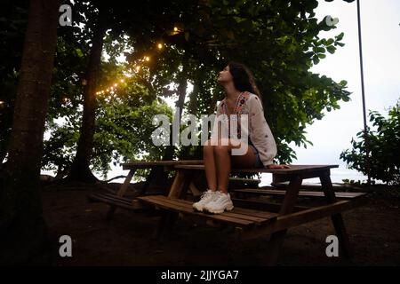 Frau, die an einem Tisch sitzt, umgeben von Licht und Natur Stockfoto