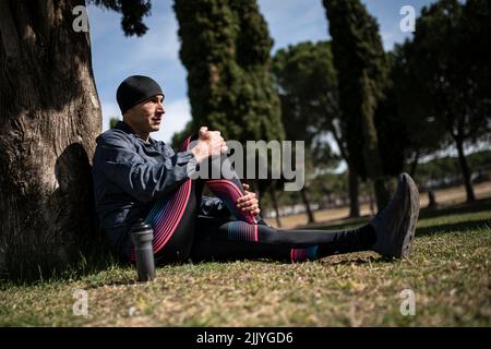 Mann, der sich im Park entspannt, auf einem Gras auf einem Baum sitzend. Stockfoto