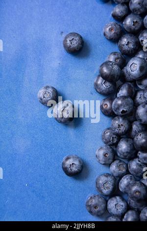 Vertikales Foto mit verstreuten Heidelbeeren auf einem blauen flachen Teller Stockfoto