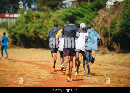 Gruppenausbildung in Kenia. Eine große Gruppe kenianischer Läufer bereitet sich auf das Rennen vor. Ausdauerläufer und Marathonprofis laufen auf dem roten Boden o Stockfoto