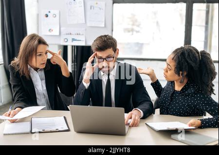 Stressiges Arbeitsumfeld. Die Kollegen werden durch die Informationen verwirrt, verlieren die Ergebnisse des Gewinns aus dem Projekt, erleben negative Emotionen, sprechen am Schreibtisch im Büro Stockfoto