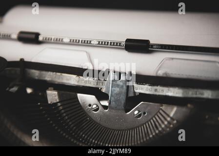 Nahaufnahme einer alten, alten Schreibmaschine mit weißem Papier im Papiereinzug mit weißer und schwarzer Tinte Stockfoto