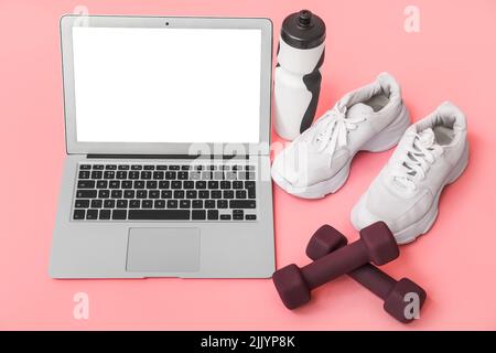 Moderner Laptop und Sportgeräte auf rosa Hintergrund Stockfoto