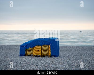 Gestapelte Plastikliegen am Strand. Liegen bei schlechtem Wetter. Resort in der Nebensaison. Seeufer Stockfoto