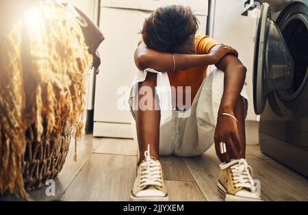 Deprimiert, müde und gestresst Teenager gelangweilt Hausarbeit zu tun. Afroamerikanisches junges Mädchen, das mit Kopfschmerzen die Wäsche macht. Genervt Stockfoto