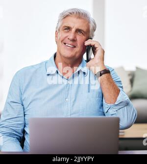 Arbeiten von zu Hause aus wie der Chef, den ich bin. Ein reifer Mann, der sein Handy und seinen Laptop benutzt, während er von zu Hause aus arbeitet. Stockfoto