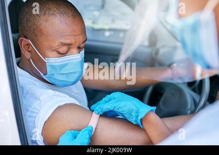 Mobiler Covid-Impfdienst im Freien für einen Patienten, der im Auto fährt. Ein Arzt, der einen Pflaster auf einen Patienten in einem Fahrzeug nach Stockfoto
